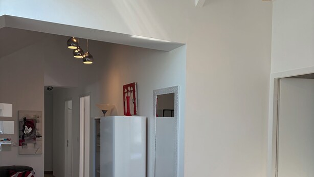 Un soggiorno moderno con zona pranzo, arredi bianchi, una lampada a soffitto e vista sul corridoio.