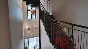 Eine Treppe mit roten Teppichstufen, schwarzen Geländern und einer hängenden Leuchte.