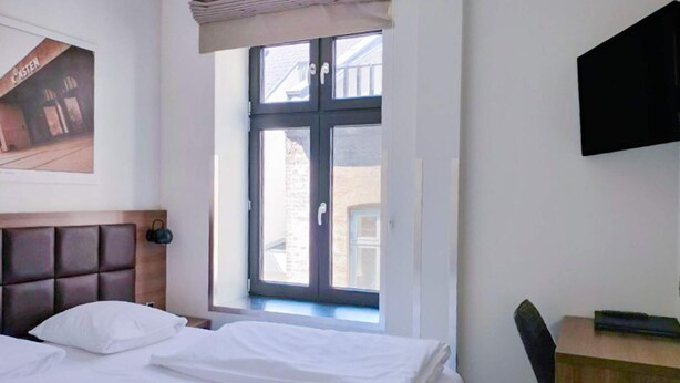 Ein Hotelzimmer mit Bett, Schreibtisch, Fernseher und Fenster mit Blick auf Gebäude.