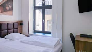 Et hotelværelse med en seng, et skrivebord, et fjernsyn og et vindue med udsigt til bygninger.