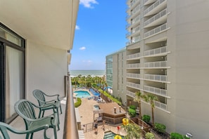 A balcony with a view of a pool and beach, a building with balconies, and a clear sky. - Beach Colony Oceanfront w/ Indoor & Outdoor Pools (Myrtle Beach)