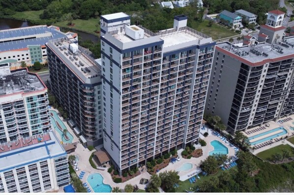 A high-rise hotel with multiple floors, a rooftop pool, and a landscaped pool area. - Beach Colony Oceanfront w/ Indoor & Outdoor Pools (Myrtle Beach)