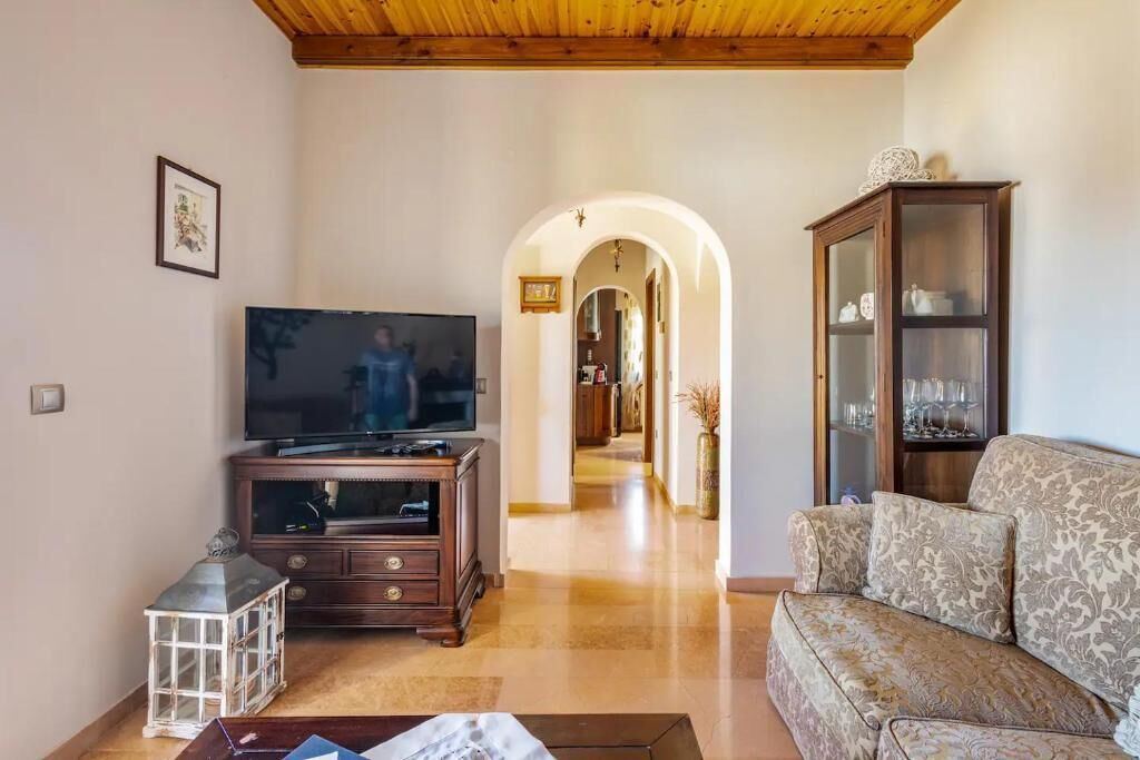 A living room with a TV, wooden entertainment unit, patterned sofa, and a cabinet with glass doors.