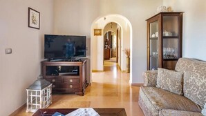 Ein Wohnzimmer mit Fernseher, Holz-Entertainment-Möbel, einem gemusterten Sofa und einer Vitrine.