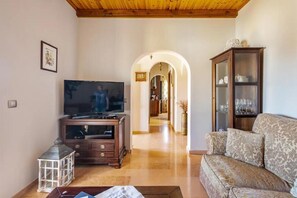 Ein Wohnzimmer mit Fernseher, Holz-Entertainment-Möbel, einem gemusterten Sofa und einer Vitrine.