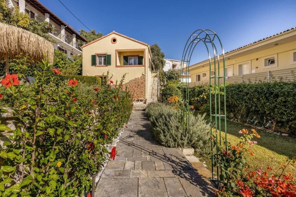 A pathway leading to a house with a stone facade, surrounded by lush greenery and flowering plants.