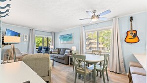 Un salon avec un canapé, une table à manger et des chaises, un ventilateur de plafond et une guitare accrochée au mur.