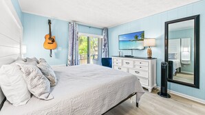 Une chambre à coucher avec un lit, une guitare, un téléviseur, une commode, un miroir et une fenêtre.