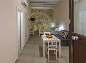 A narrow hallway leading to a bedroom with a stone wall, a bed, a bedside table with a lamp, and a small table with a bowl of fruit. - Essentia Ortigia Rooms Earth - Apartment Wifi (Siracusa)