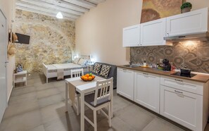 A compact kitchen with white cabinets, a dining table with chairs, a stone wall, and a ceiling with exposed beams. - Essentia Ortigia Rooms Earth - Apartment Wifi (Siracusa)