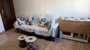 A sofa with floral cushions, a small wooden table, and two round stools. - Cozy Apartment in the Center of Avilés- Next to the Historic Center and Niemeyer (Avilés)