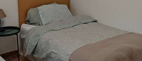 A single bed with a wooden headboard, a bedside table with a lamp, and a patterned rug on a tiled floor.
