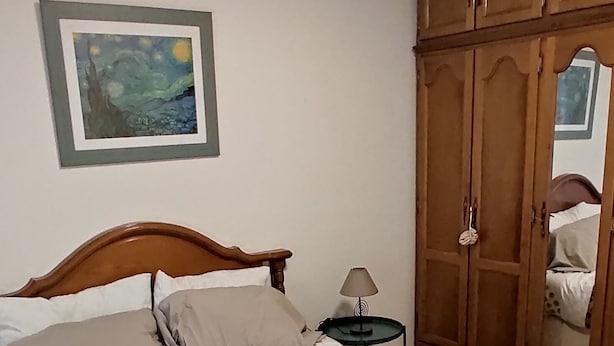 A neatly made bed with a patterned bedspread, a wooden wardrobe, a framed artwork on the wall, and a lamp on a bedside table. - Cozy Apartment in the Center of Avilés- Next to the Historic Center and Niemeyer (Avilés)