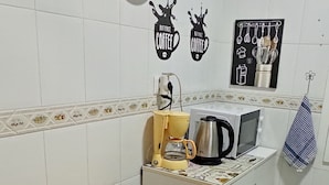 A small kitchen with white tiles, a wooden table, a clock, and coffee-making equipment. - Cozy Apartment in the Center of Avilés- Next to the Historic Center and Niemeyer (Avilés)