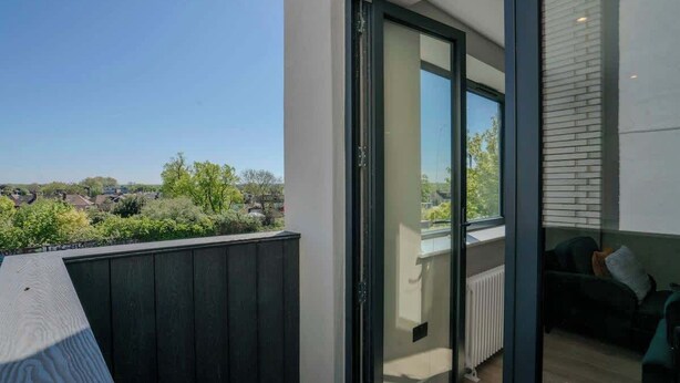 En modern lägenhet med balkong, en skjutdörr i glas och utsikt över ett bostadsområde.