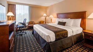A hotel room with a bed, desk, chair, lamps, and a view of the outdoors. - Lower South End (Charlotte)