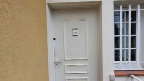 Une porte blanche avec une plaque portant un numéro, une fenêtre aux montants blancs et un paillasson avec du texte.