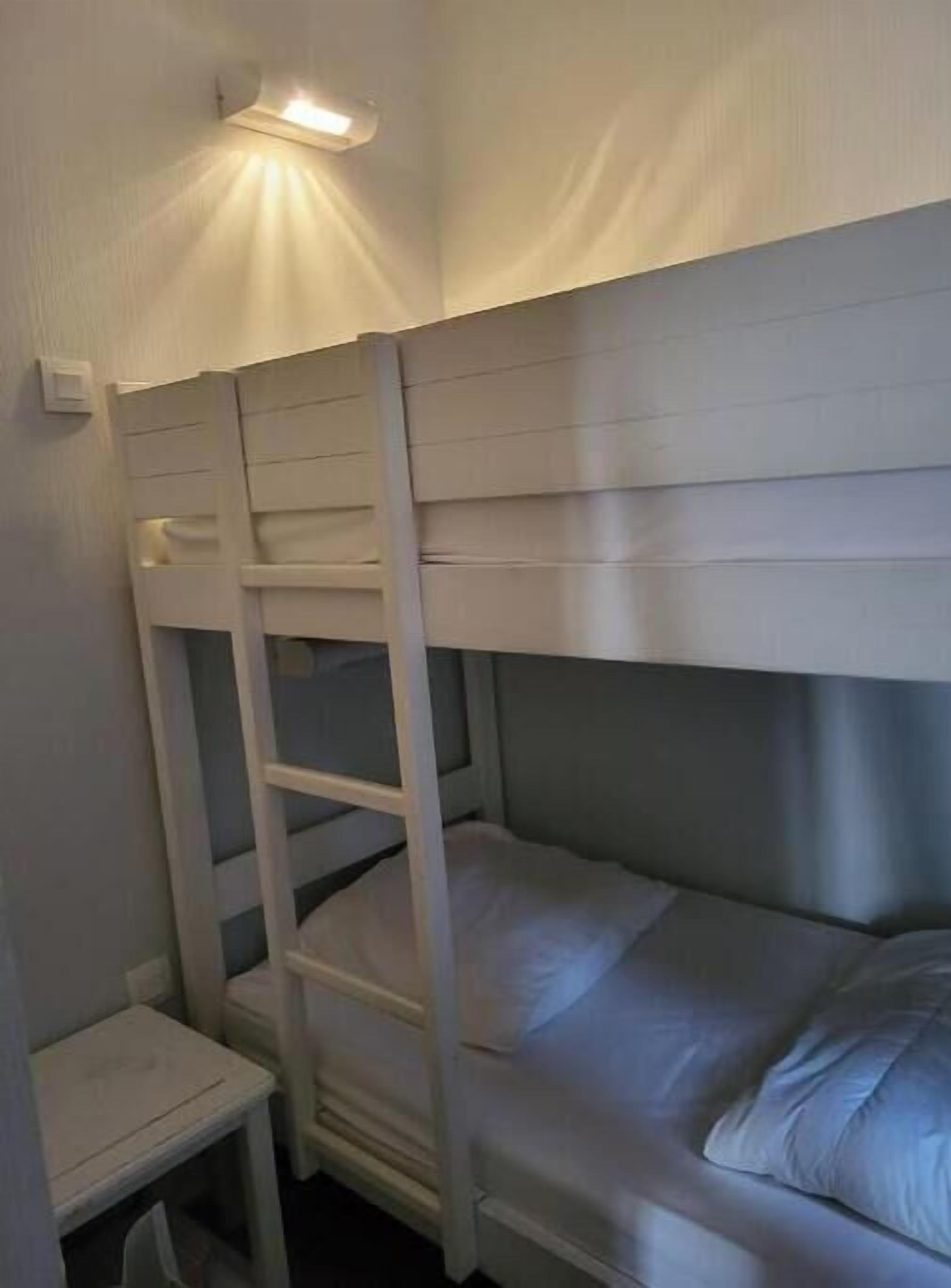 A bunk bed with a ladder, a small table, and a wall-mounted light fixture.