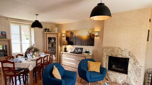 A dining area with a table set for four, a fireplace, and blue chairs. - Charming retreat, pets welcome - 8 guests (La Chapelle-Saint-Martin-en-Plaine)