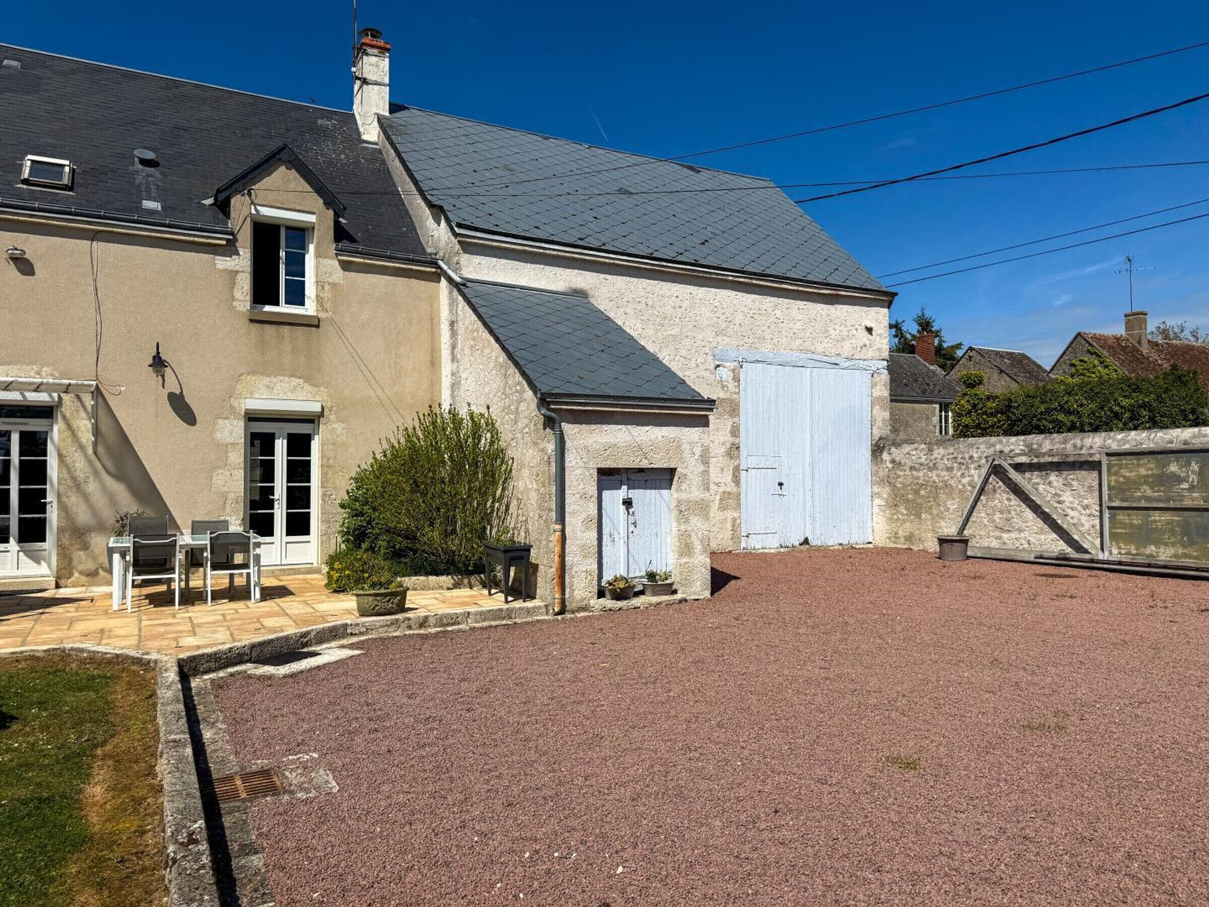 A two-story house with a gravel driveway, a small patio with outdoor furniture, and a large window.