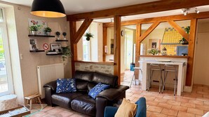 A living room with a leather sofa, a blue armchair, and a glass coffee table. There is a kitchen visible in the background with a bar counter and stools. - Charming retreat, pets welcome - 8 guests (La Chapelle-Saint-Martin-en-Plaine)