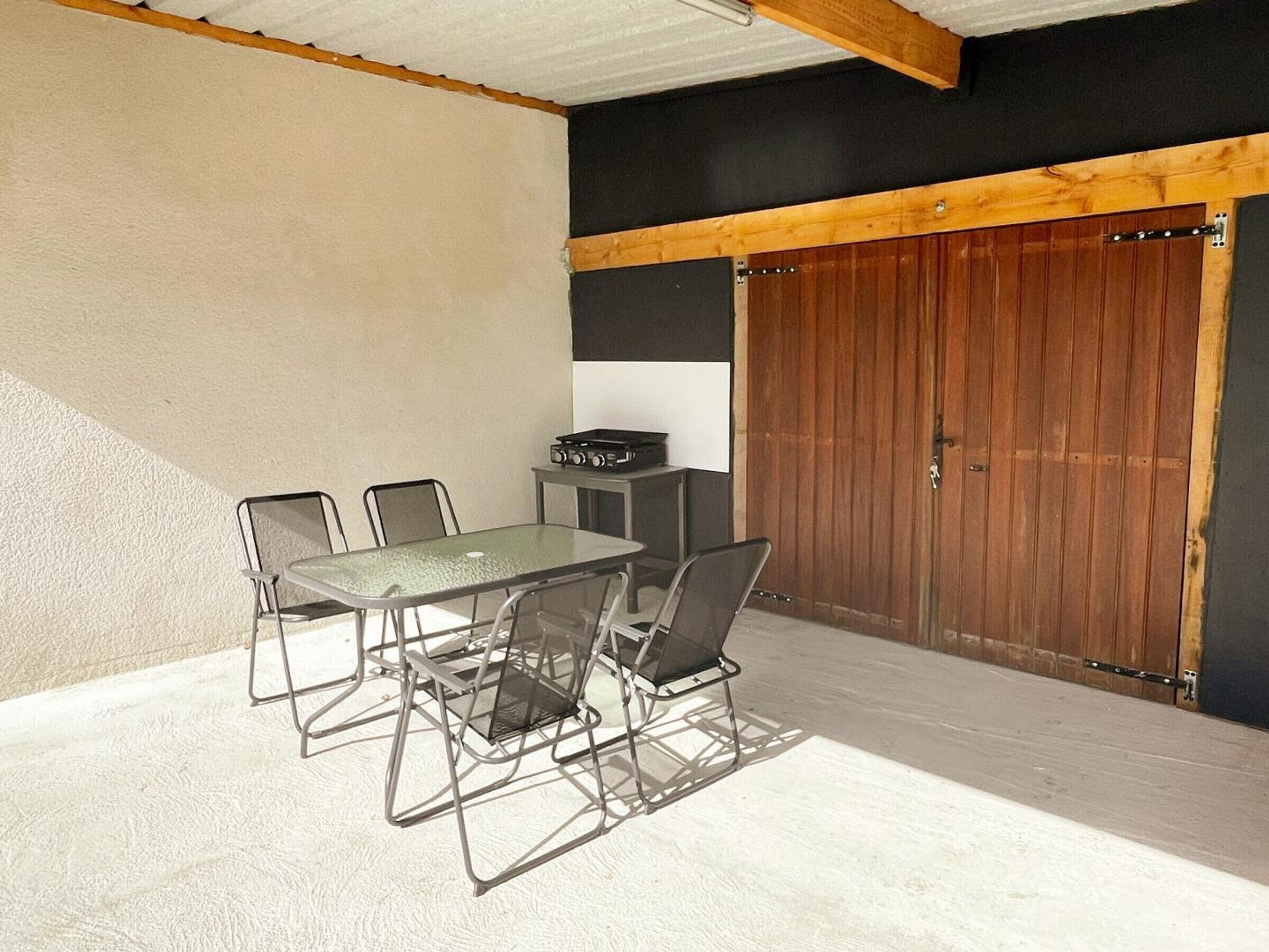 A covered patio area with a table and chairs, a grill, and a wooden door.