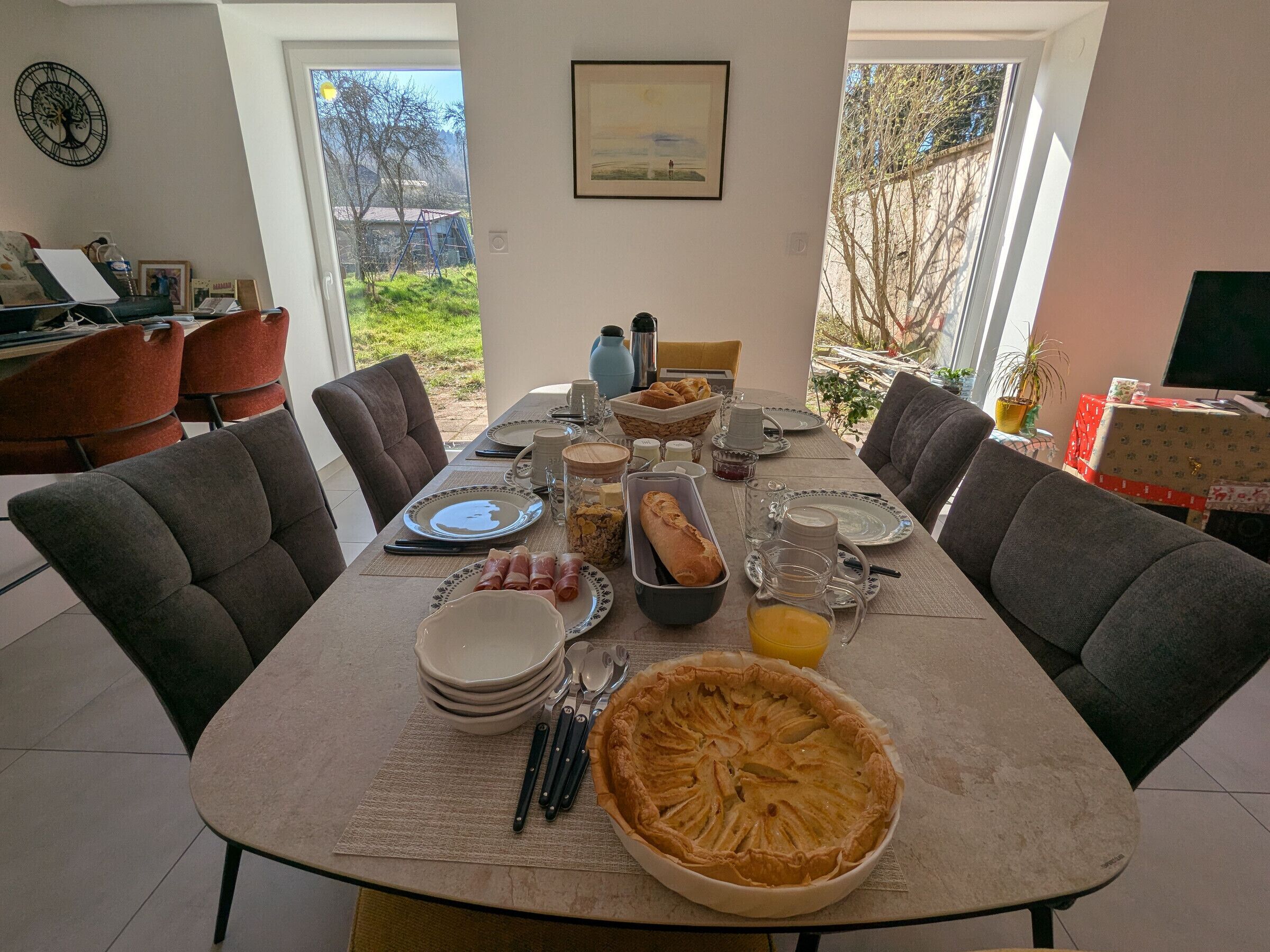 A dining table set with plates, cutlery, a pie, and a loaf of bread, with chairs around it.