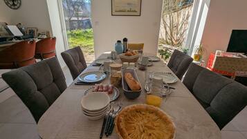 A dining table set with plates, cutlery, a pie, and a loaf of bread, with chairs around it.