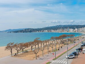 Eine Küstenstadt mit Strand, einer Straße mit geparkten Autos und einem Fußgängerweg.