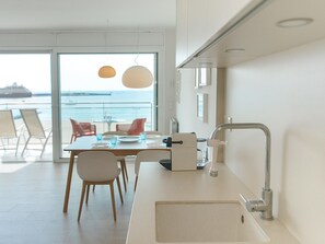 Eine moderne Küche mit einem großen Fenster, einem Essbereich mit Stühlen und Blick aufs Meer.