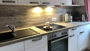 Una cucina moderna con mobili bianchi, lavello in acciaio inossidabile, forno integrato e un piano di lavoro con bollitore e macchina da caffè.