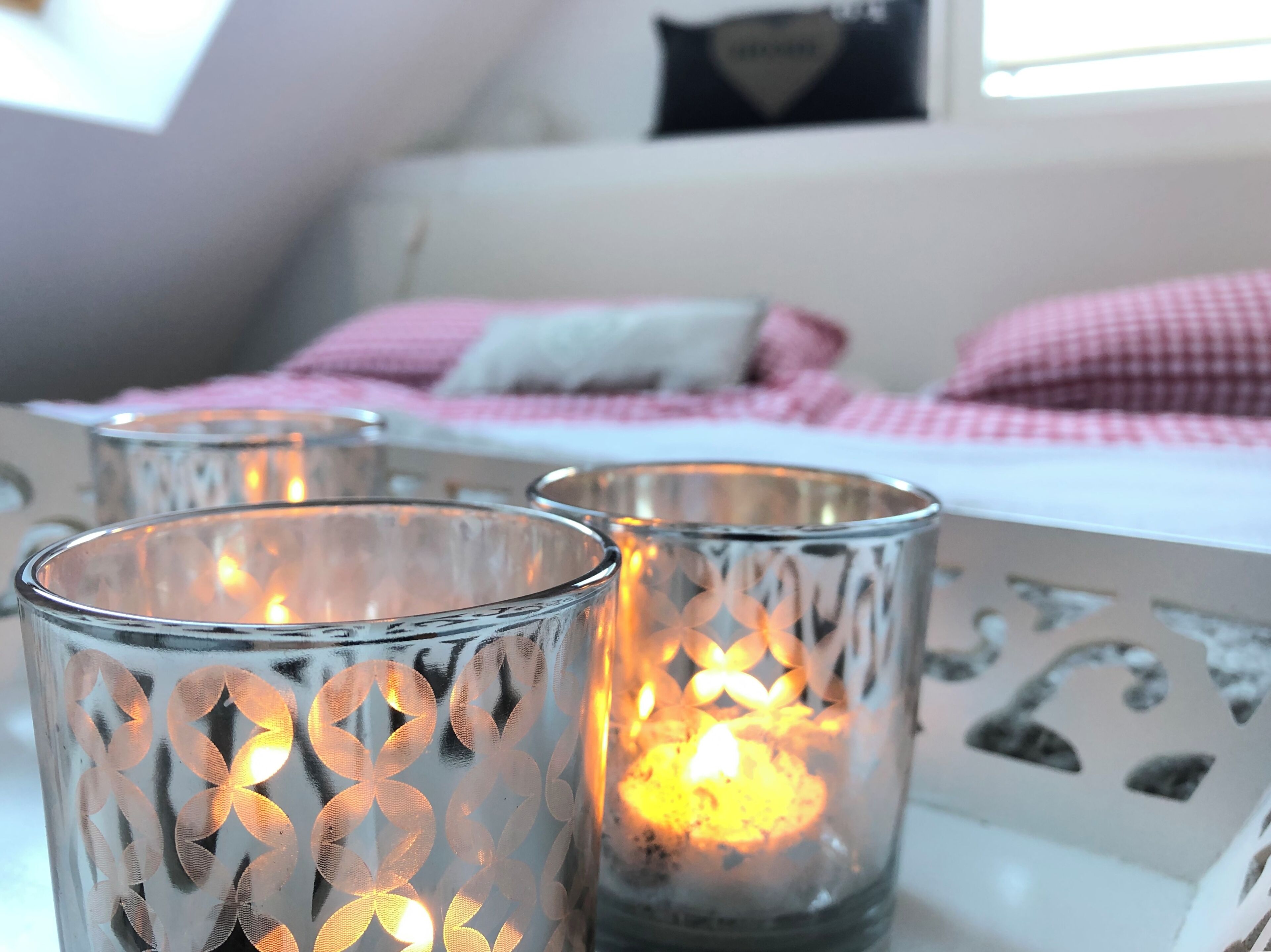 Una habitación con una cama, una mesa blanca y tres velas encendidas con diseños decorativos.