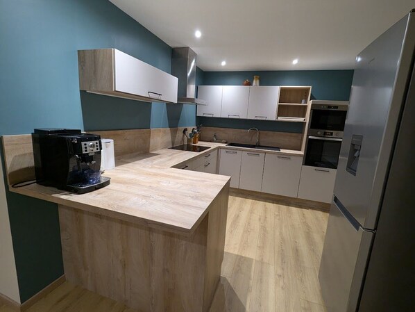 Une cuisine moderne avec des meubles de couleur bois clair, un îlot central intégré et des appareils électroménagers en acier inoxydable.