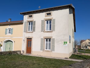 A two-story building with a central entrance door, shuttered windows, and a small balcony.