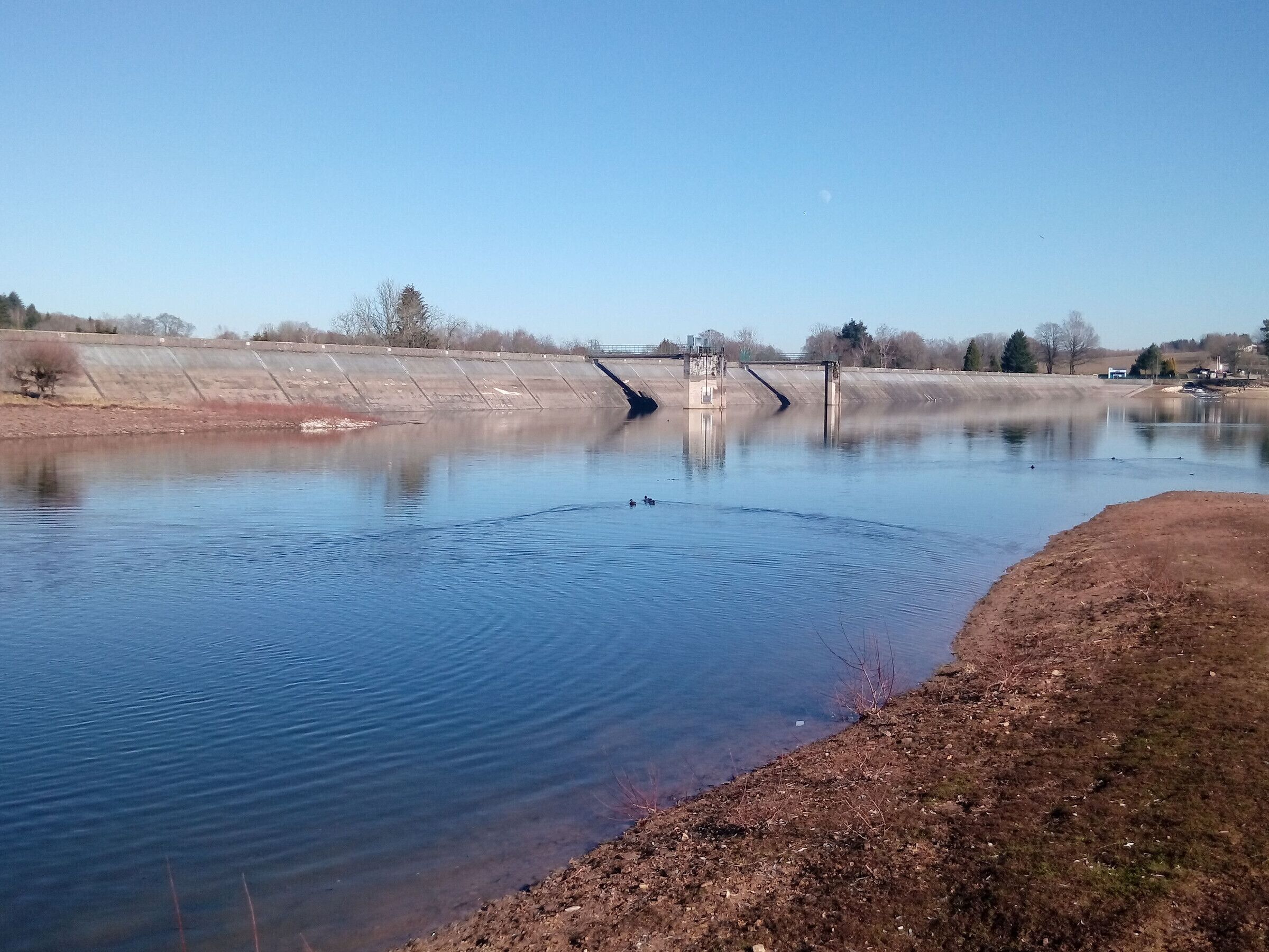 Une rivière paisible, avec un barrage, et un ciel dégagé.