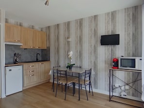 A modern kitchen with wooden cabinets, a dining table with chairs, a microwave, and a small TV on the wall. - Charming apartment with WiFi - 4 guests (Prémanon)