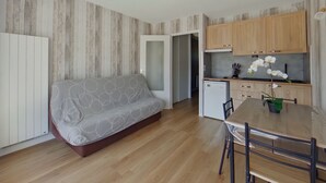 Um espaço compacto para viver, com sofá, mesa de jantar e cadeiras, pequena cozinha e ventilador de teto.