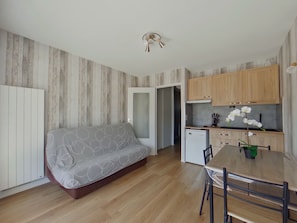 A compact living space with a sofa, a dining table with chairs, a small kitchenette, and a ceiling fan. - Charming apartment with WiFi - 4 guests (Prémanon)