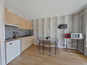 A modern kitchen with wooden cabinets, a built-in microwave, and a dining table with chairs. - Charming apartment with WiFi - 4 guests (Prémanon)