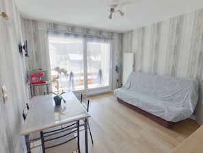 A modern living room with a sofa, a dining table, and a large window. - Charming apartment with WiFi - 4 guests (Prémanon)