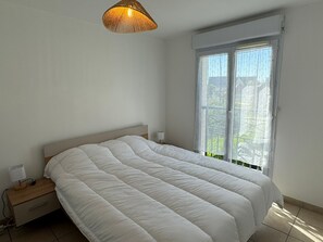 Ein Schlafzimmer mit Bett, Nachttisch, Lampe, einem Fenster mit Vorhängen und einer Pendelleuchte.