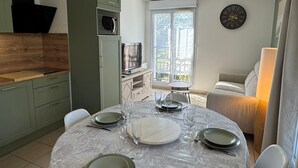 Ruokailutilassa on pyöreä pöytä, johon on katettu neljälle, mikroaaltouuni ja seinällä oleva kello.