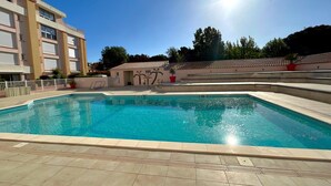 Una piscina con solárium empedrado, un edificio con amplias ventanas y un cielo despejado.