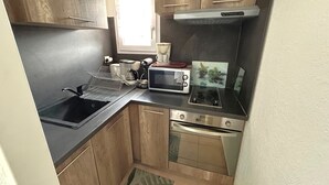 Una cocina compacta con un lavamanos, microondas, estufa y una ventana con cortinas.