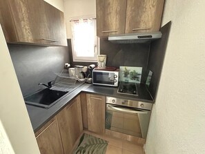Eine kleine Küche mit Spüle, Mikrowelle, Herd und einem Fenster mit Vorhängen.