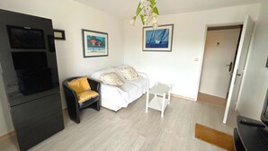 Una sala de estar con un sofá, una mesita, un mueble negro para televisor y una puerta que da a otra habitación.