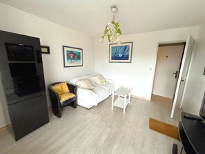 Ein Wohnzimmer mit einer Couch, einem kleinen Tisch, einer schwarzen TV-Konsole und einer Tür zu einem anderen Raum.