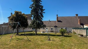A residential property with a fenced yard, a swing set, a tall coniferous tree, and a house with a tiled roof.