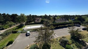 Un parking avec une voiture blanche, entouré de verdure et de maisons.