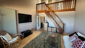Un salon avec un escalier en bois, un téléviseur à écran plat, un fauteuil à bascule, une table basse en verre et un canapé agrémenté de coussins à motifs.